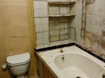 Before renovation: outdated bathroom with old fixtures, worn tiles, and poor lighting